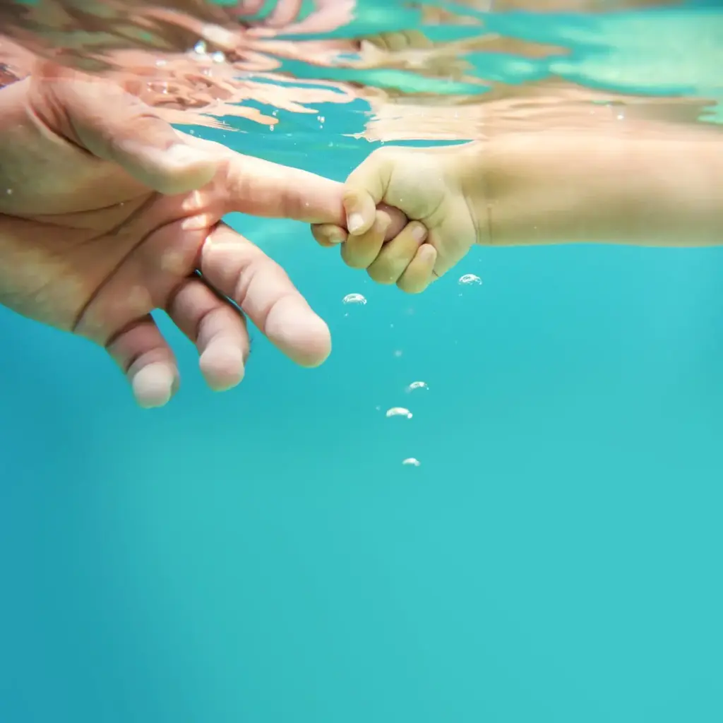 Unterwasseraufnahme von zwei Händen – symbolisiert Vertrauen, Geborgenheit und Gesundheit.
